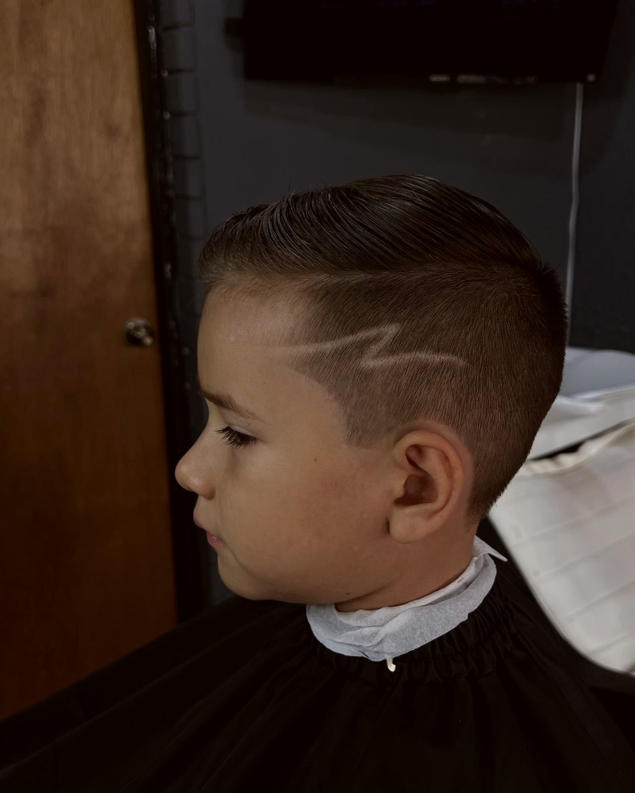 Niño con corte degradado y diseño de rayo en el costado